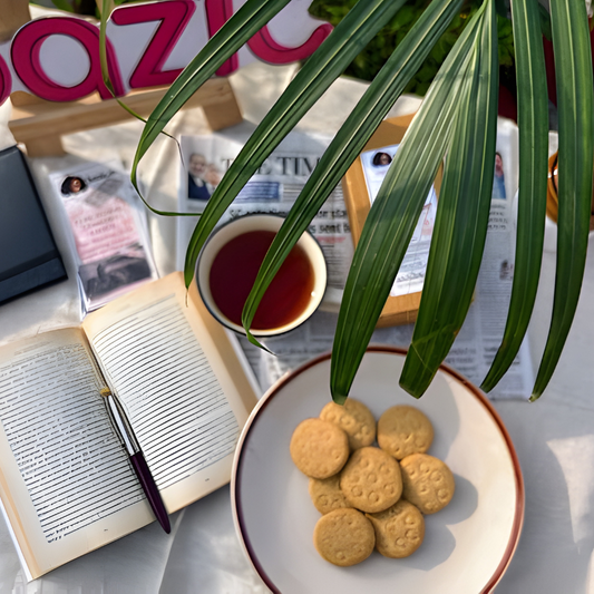 Jowar Ajwain Jaggery Butter Cookies in open kraft box with sorghum grain and ajwain seeds on dark slate surface